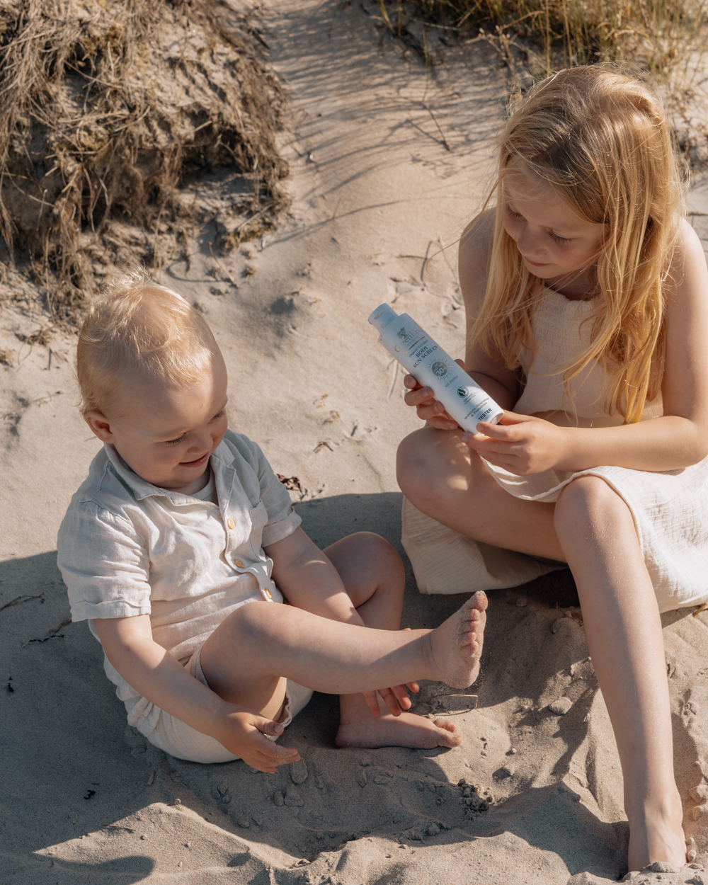 två barn en yngre pojke och en äldre flicka på en strand med ekologisk produkt från greenetiq